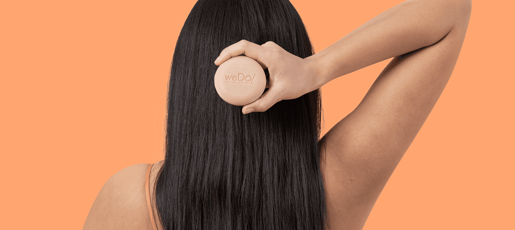 Parte posteriore della testa di donna con lunghi capelli neri, con in mano la barra shampoo senza plastica di weDo/