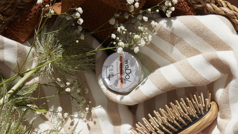 pot of Protect Balm from weDo Professional, next to a brush and wildflowers