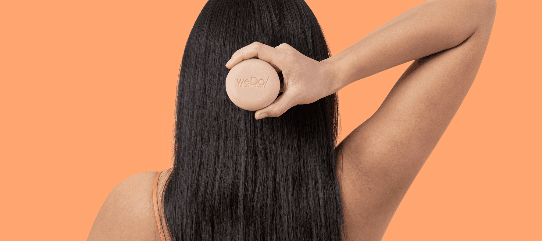 Parte posterior de la cabeza de la mujer con cabello largo y negro , sosteniendo el champú sólido No Plastic de weDo/